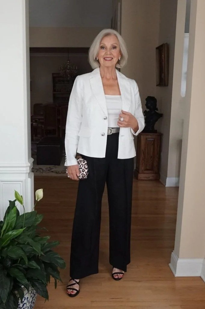 plus-size white-haired woman wearing white blazer with black palazzo trousers indoors