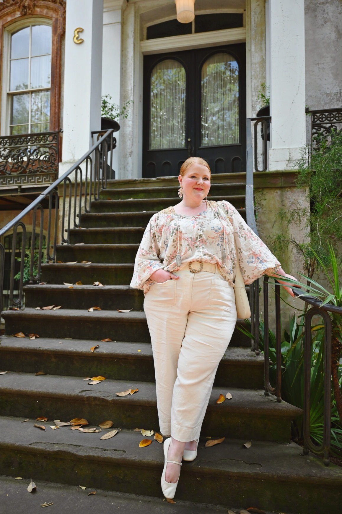 plus-size woman over 60 wearing cream floral blouse with white pull-on trousers on staircase