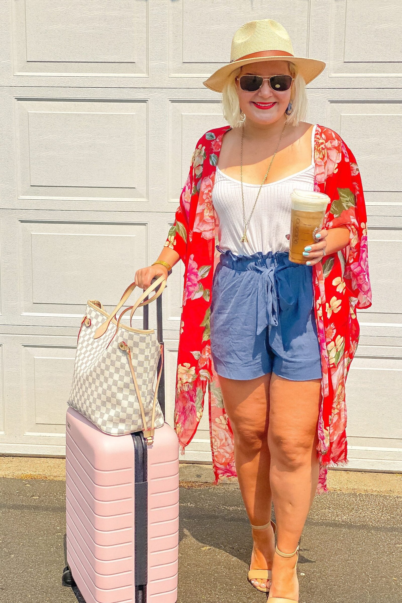 plus-size woman over 60 wearing red floral kimono over denim shorts with pink suitcase