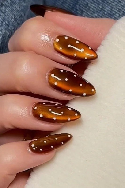 Amber cat-eye almond nails with white polka dots styled with a denim jacket