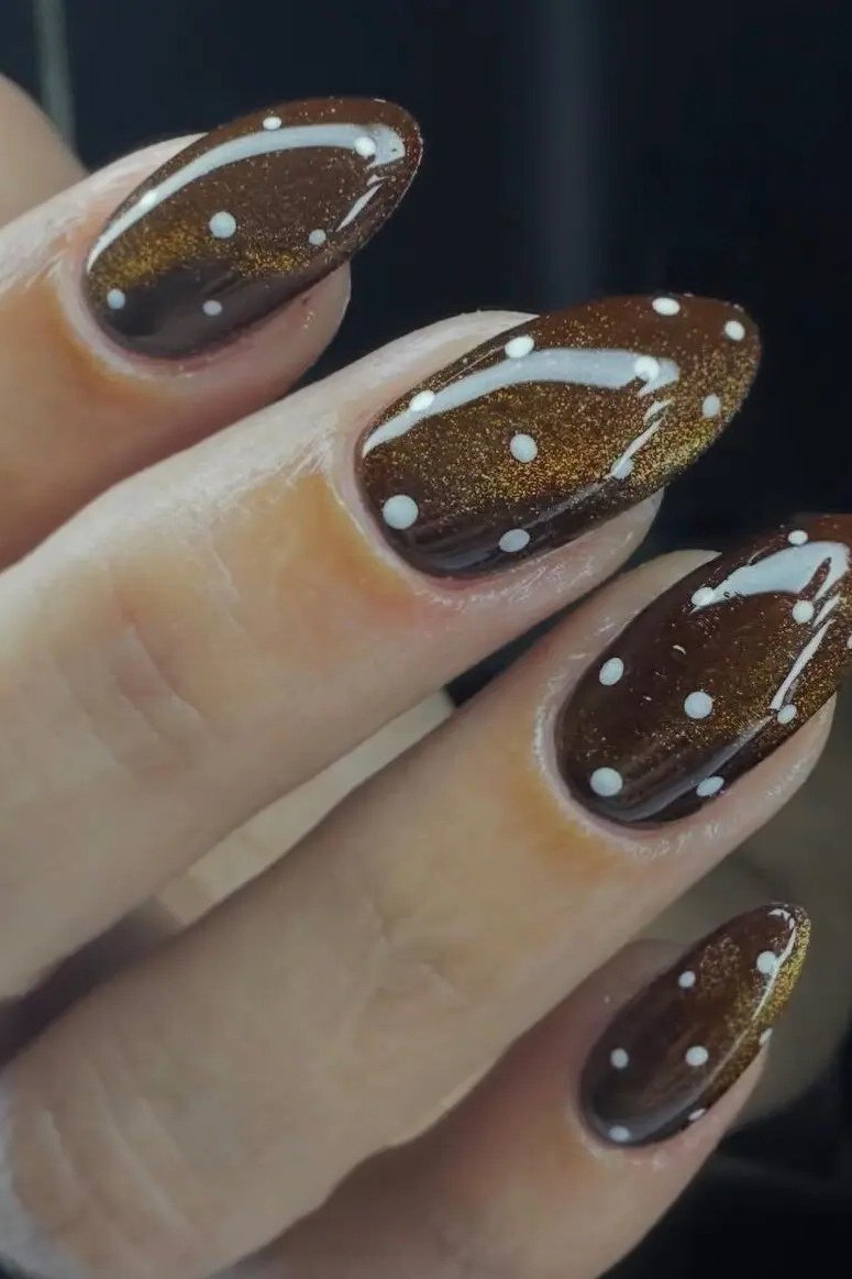 Deep chocolate cat-eye almond nails with white polka dots close up