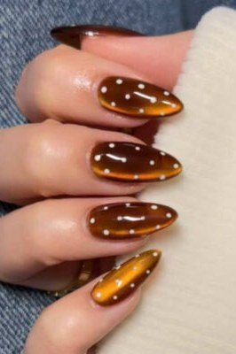 Amber and caramel cat-eye almond nails with white polka dots, cozy fall nail art