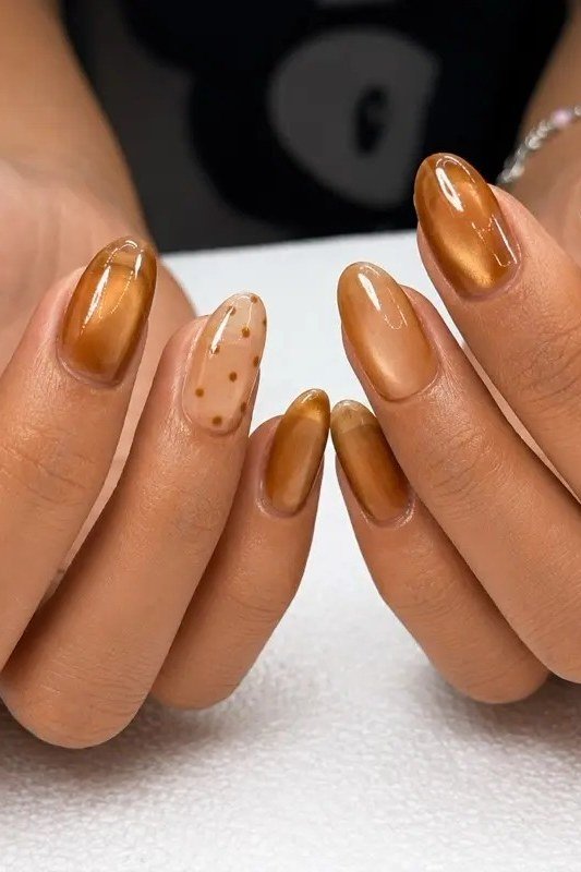 Amber gold cat-eye almond nails with white polka dot accents on both hands