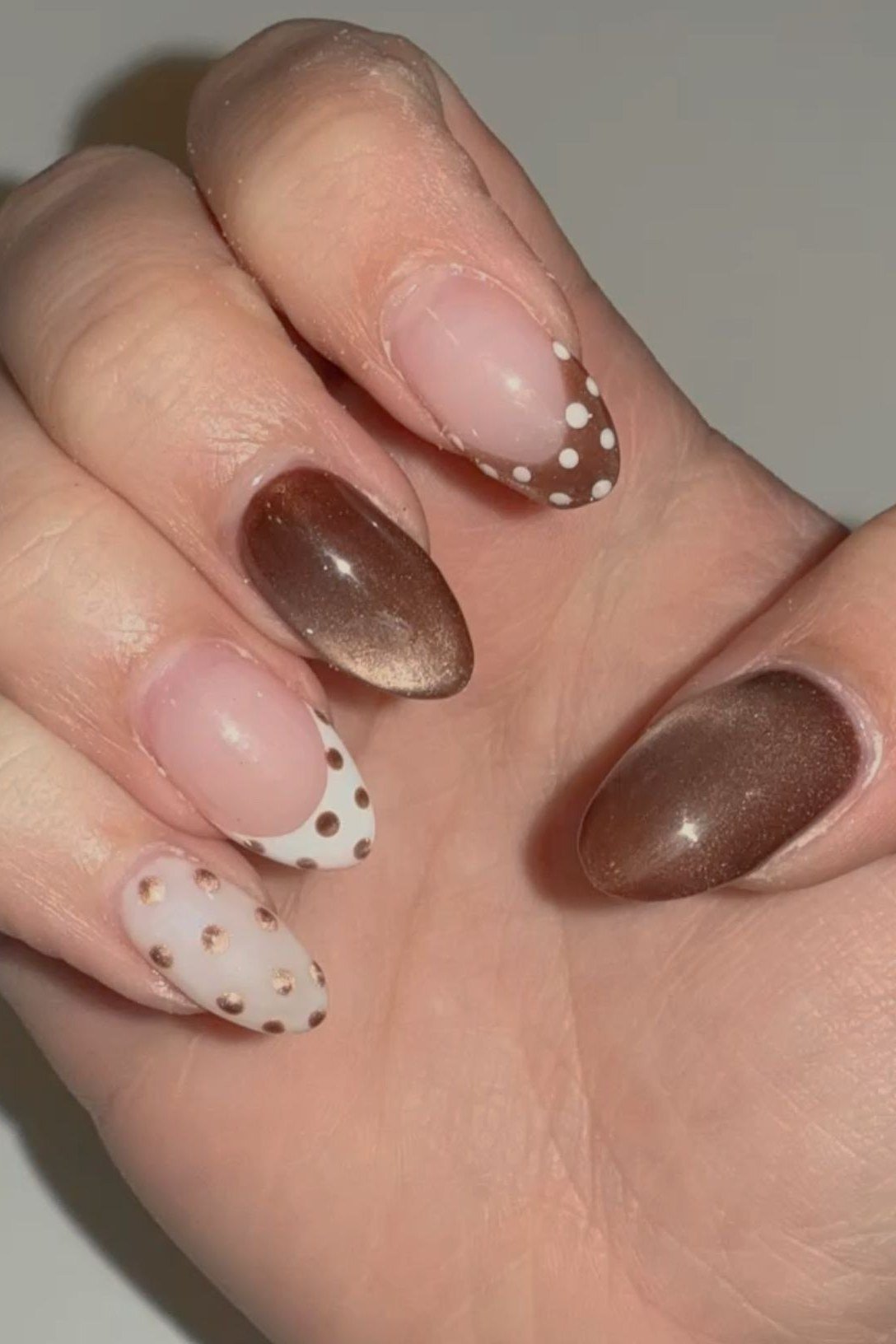 Chocolate cat-eye almond nails beside white nails with brown polka dots, fall nail design