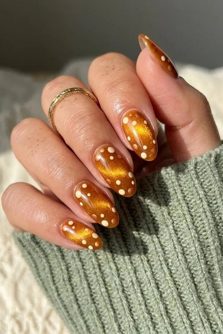Amber cat-eye stiletto nails with white polka dots styled with a green knit sweater