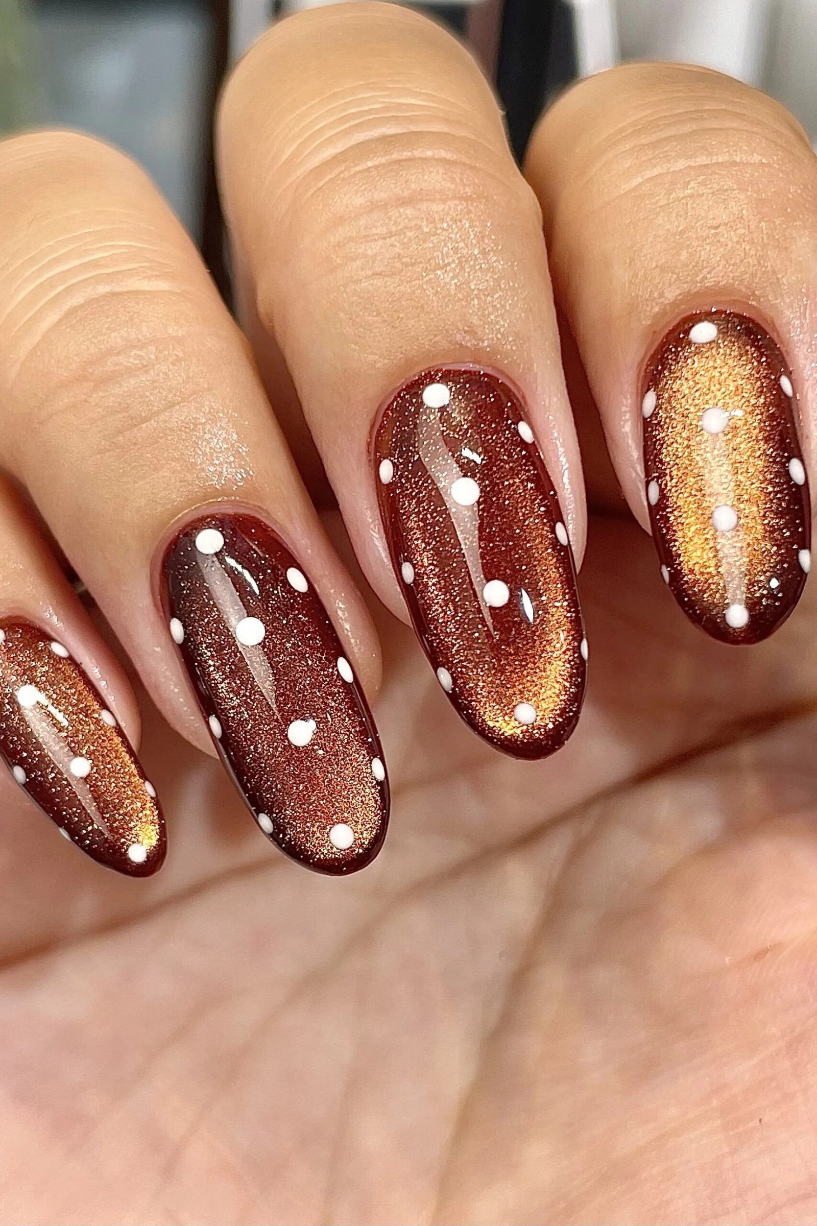 Copper cat-eye almond nails with white polka dots close up in warm light