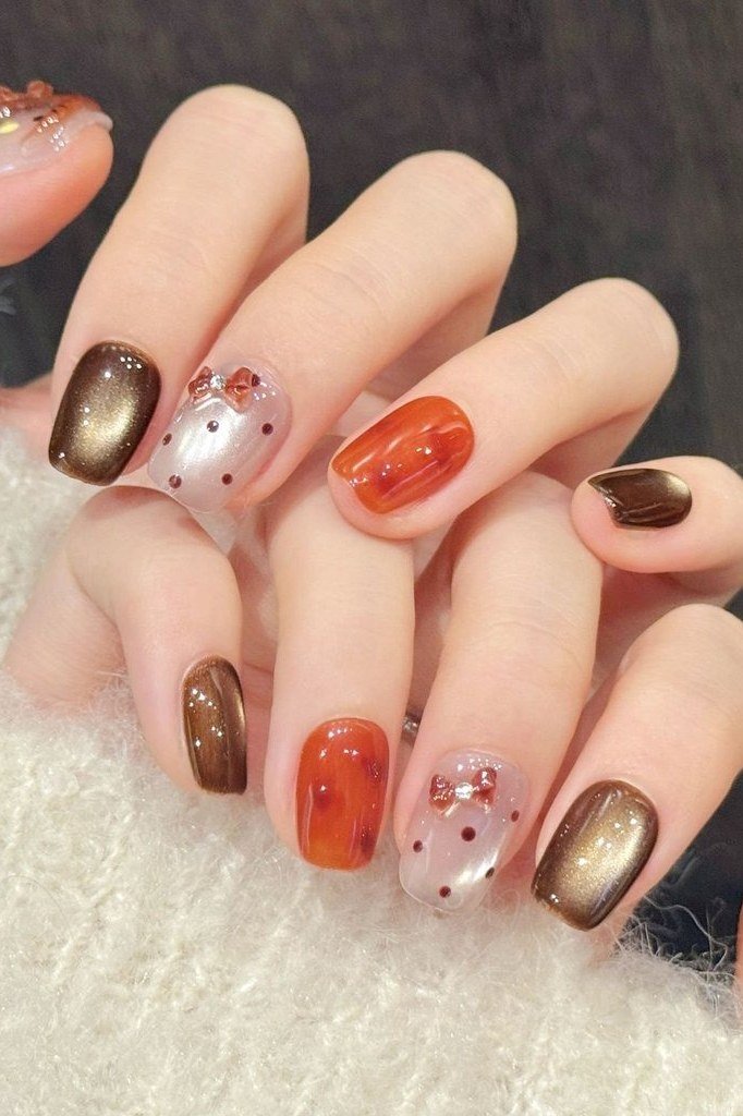 Burnt orange and bronze cat-eye nails with a white polka dot bow accent nail, fall nail art
