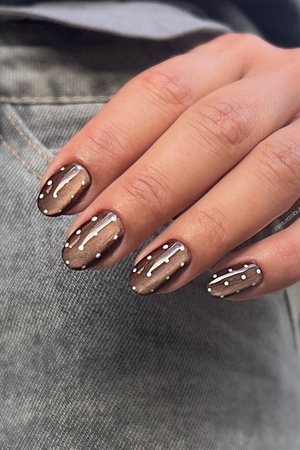 Bronze cat-eye almond nails with white polka dots styled with denim