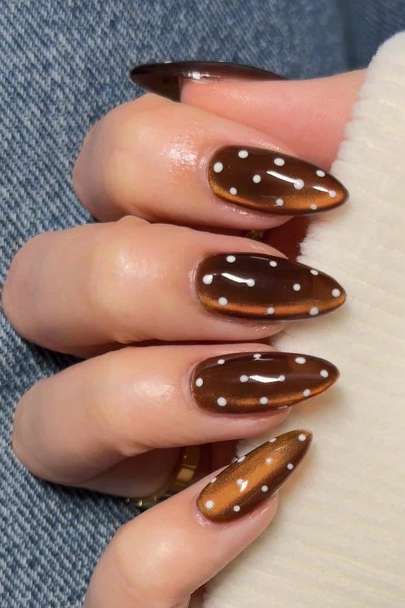 Amber cat-eye almond nails with white polka dots and a denim jacket, fall nail design