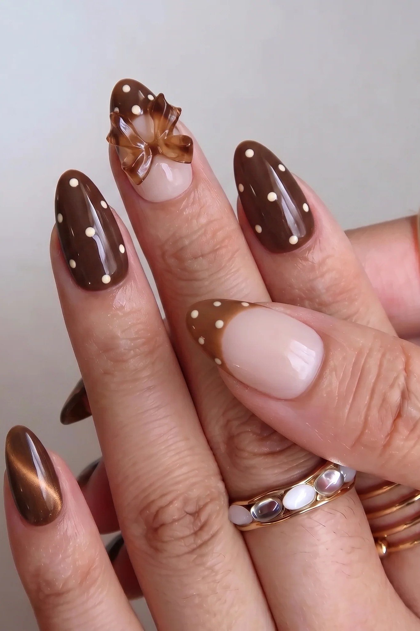 Chocolate cat-eye almond nails with white polka dots and a nude bow accent nail
