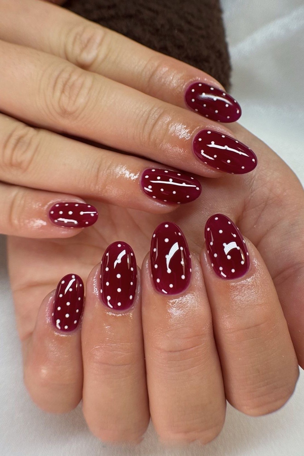 Oxblood almond nails with white polka dots on both hands, fall nail design for women over 50