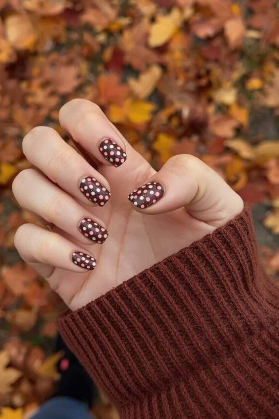 Burgundy short nails with white polka dots resting on fall leaves