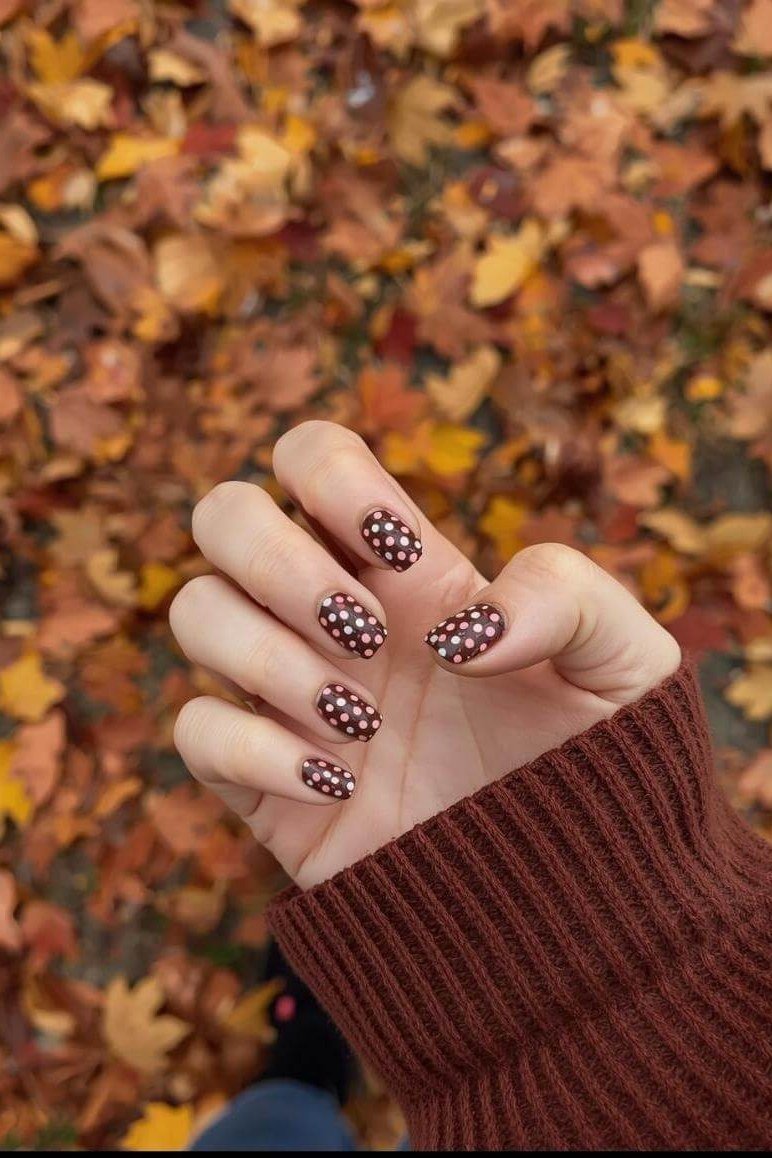 Burgundy short nails with white polka dots above autumn leaves, fall nail design