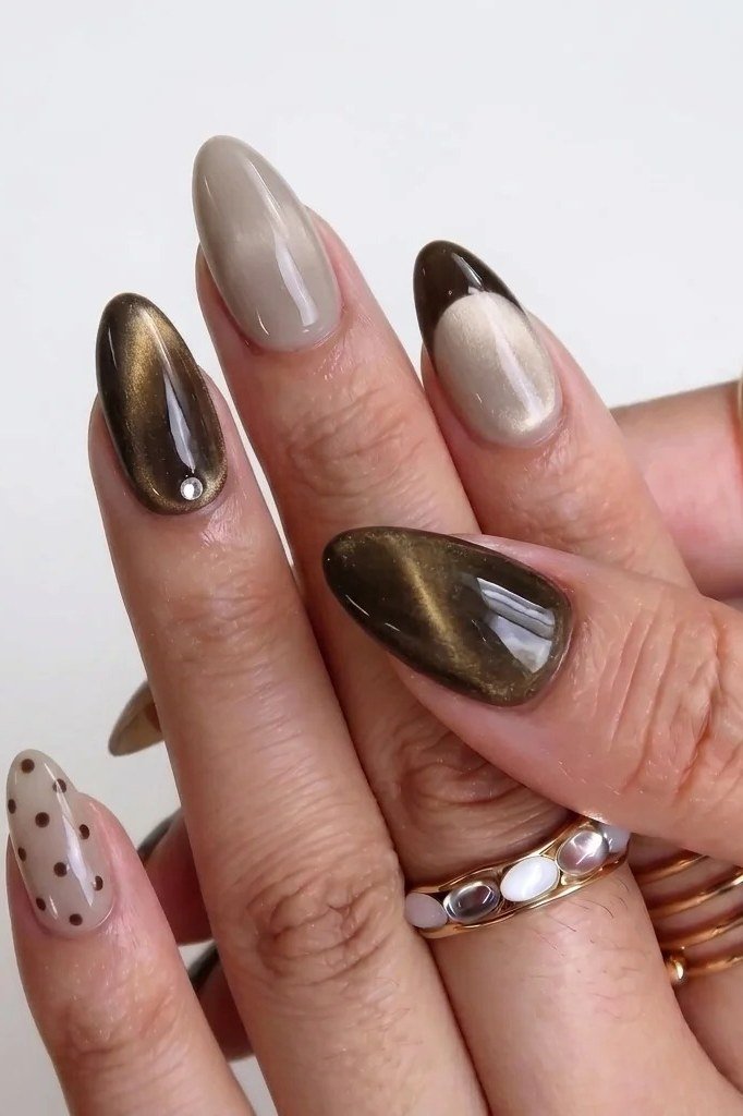 Bronze cat-eye almond nails with a nude polka dot accent nail and rings
