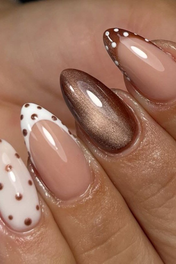 Nude almond nails with bronze cat-eye French tips and white polka dots close up