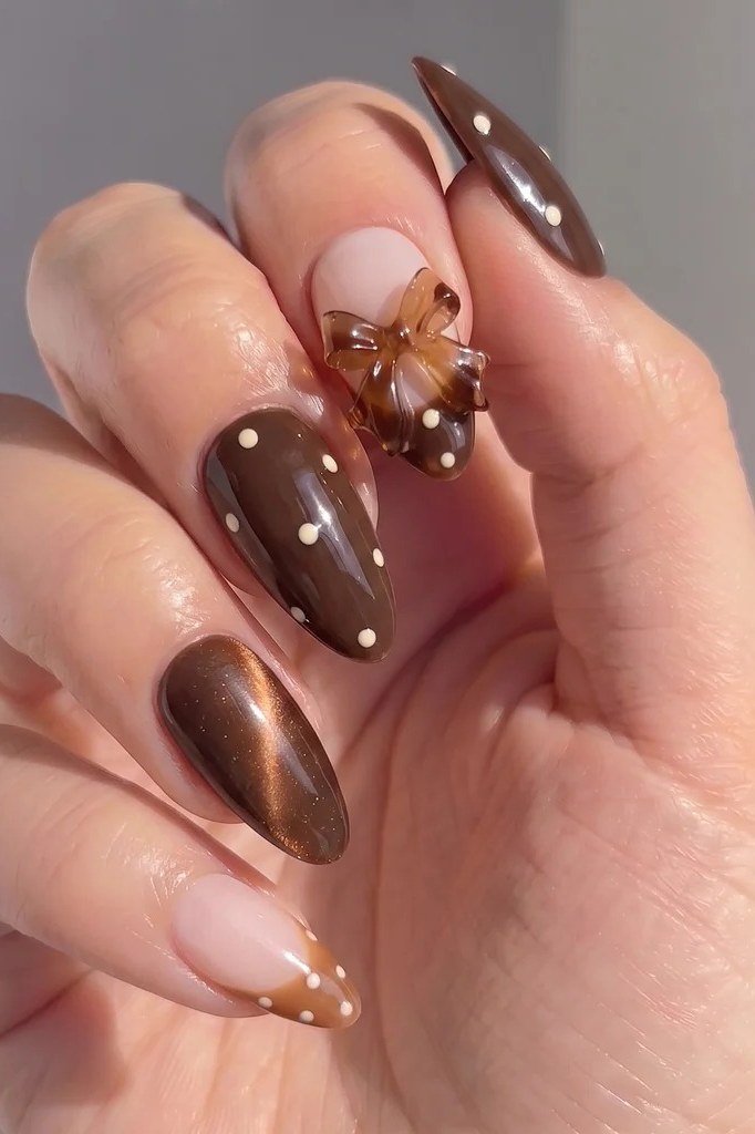 Chocolate stiletto nails with white polka dots and a nude bow accent nail