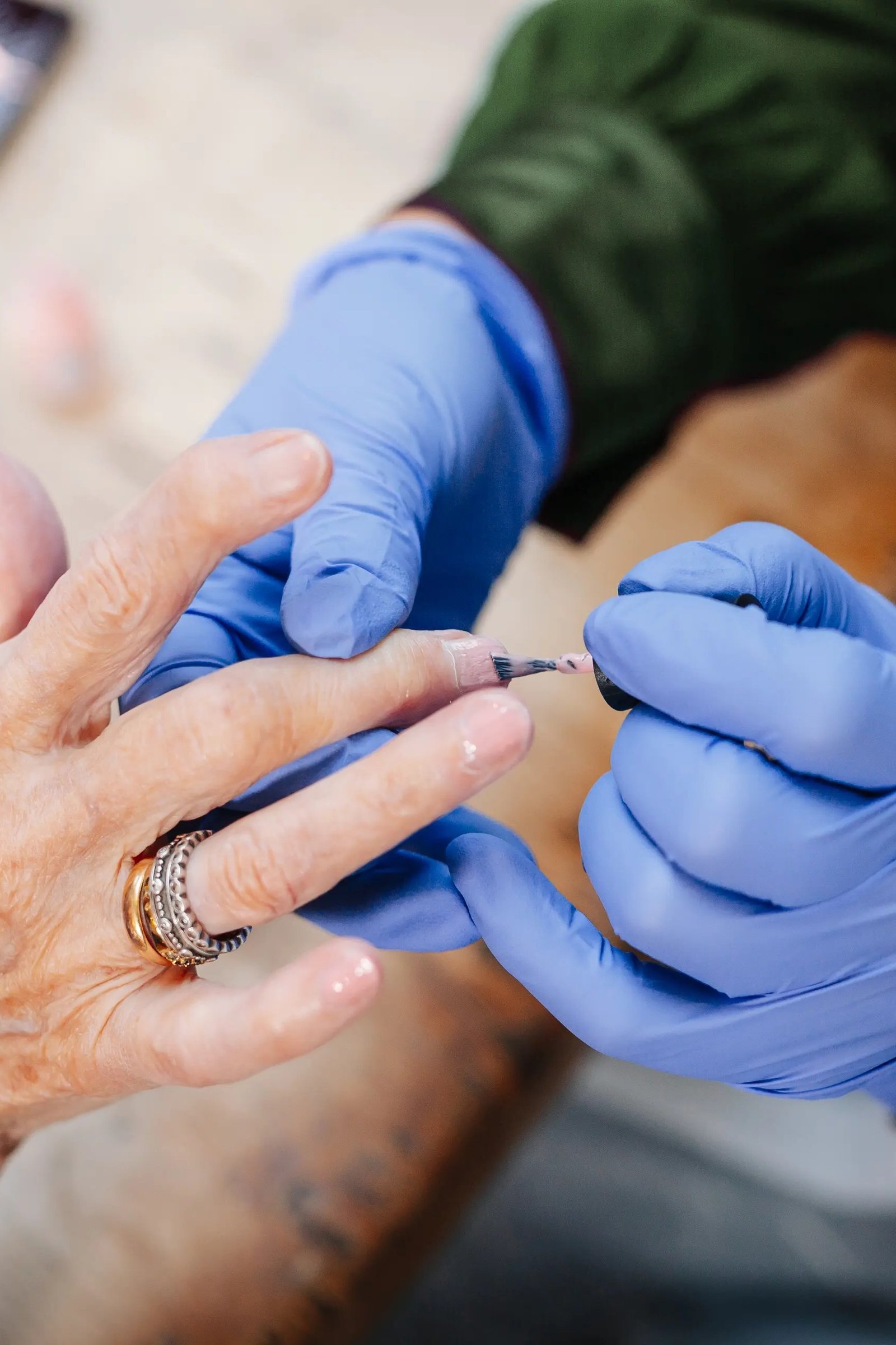 Nail technician in blue gloves applying a press-on nail to an elderly woman's hand