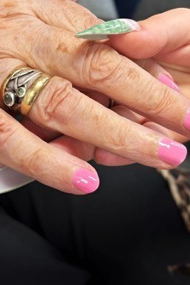 Close-up of a press-on nail being pressed onto an elderly woman's pink-tipped finger