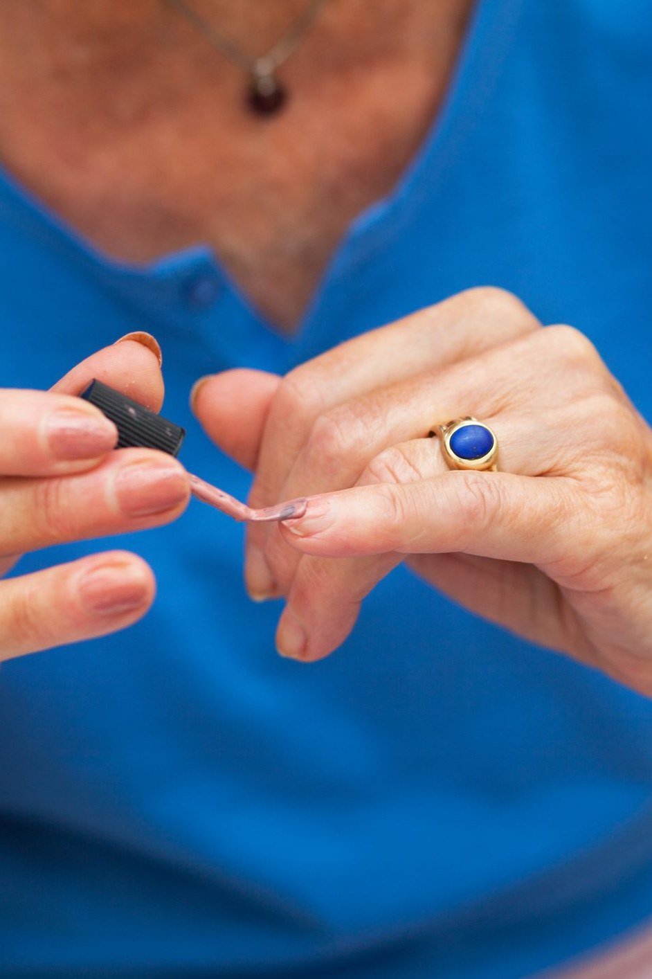 Older woman in a blue top applying a press-on nail to her own hand