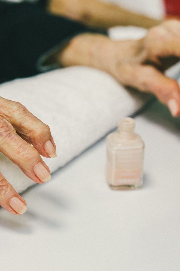 Salon nail care on an elderly woman's hand with a bottle of polish nearby