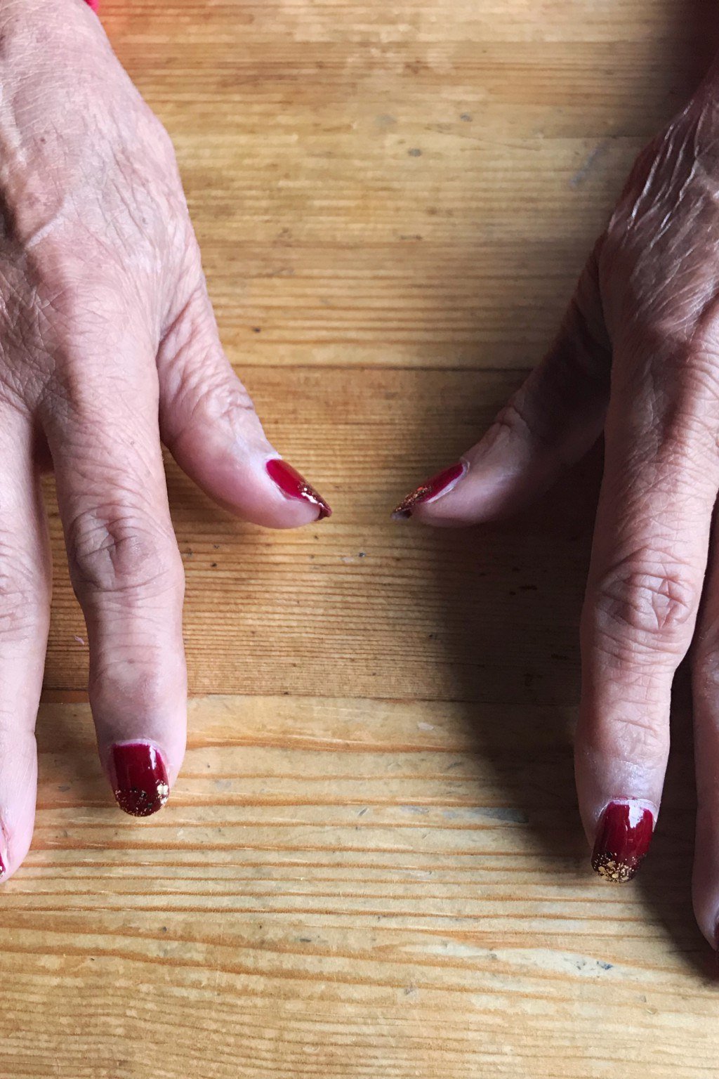 Two mature hands with burgundy nails on a wooden table
