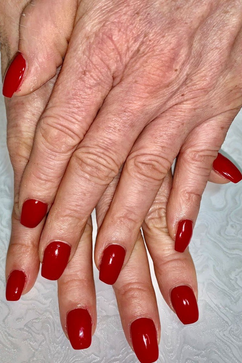 Elderly crossed hands with classic glossy red nails