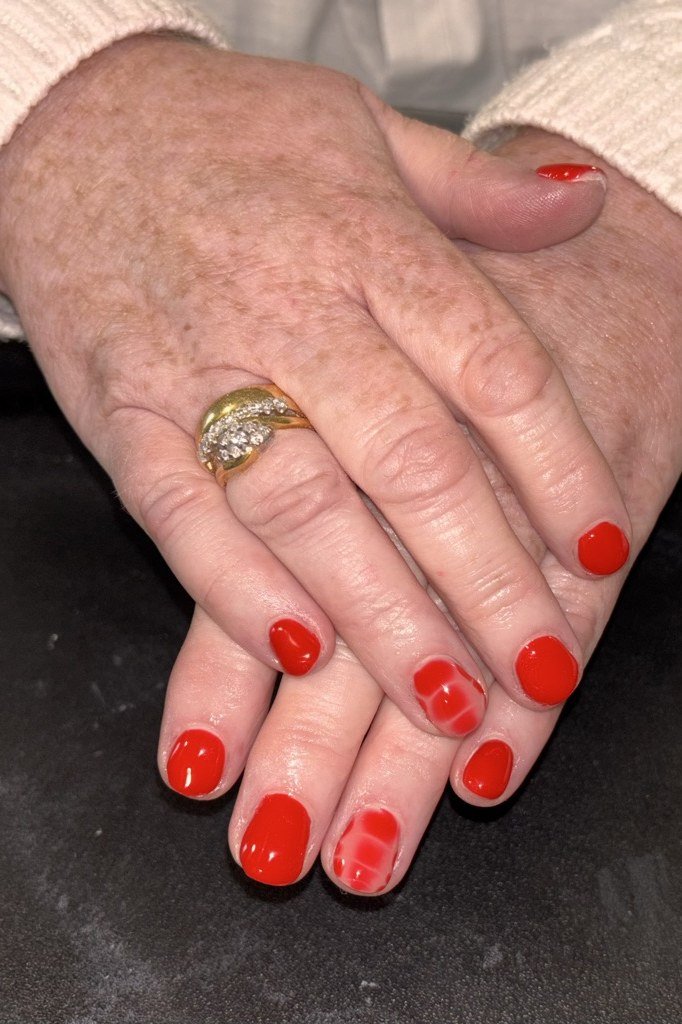 Mature crossed hands with red-orange nails and a gold ring