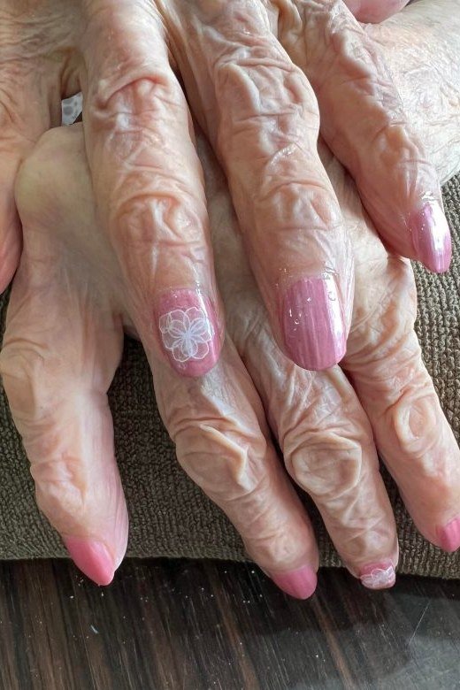 Elderly crossed hands with pink nails and a floral accent nail