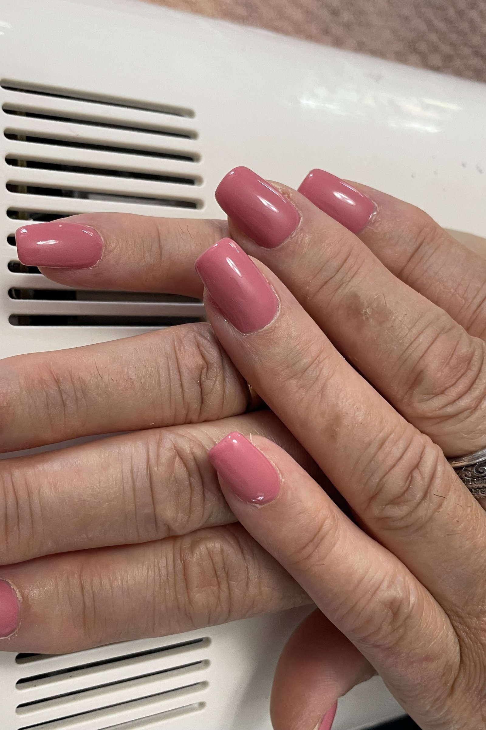 Mature hands with mauve-pink nails under a UV lamp (press-on curing)
