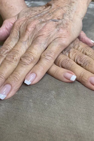 Elderly crossed hands with French tips on gray fabric