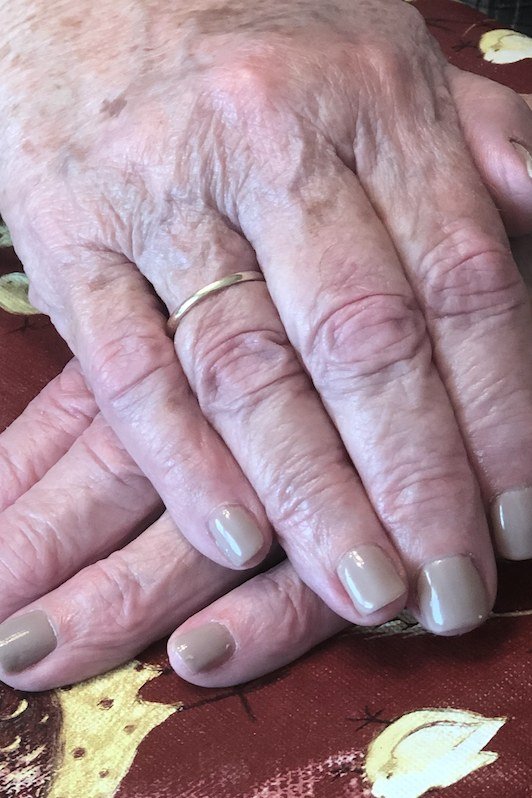 Elderly hands with gray-taupe nails on a patterned tablecloth
