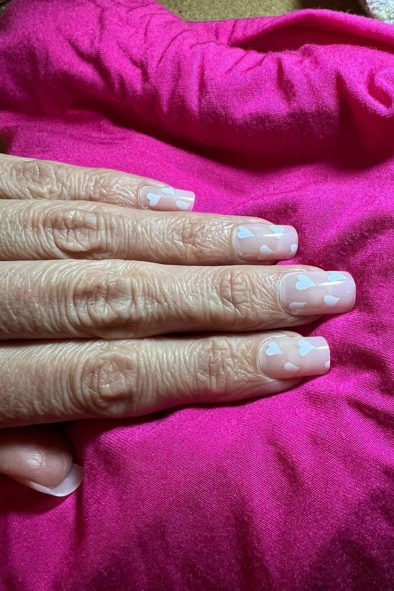 Mature hands with nude nails resting on magenta fabric