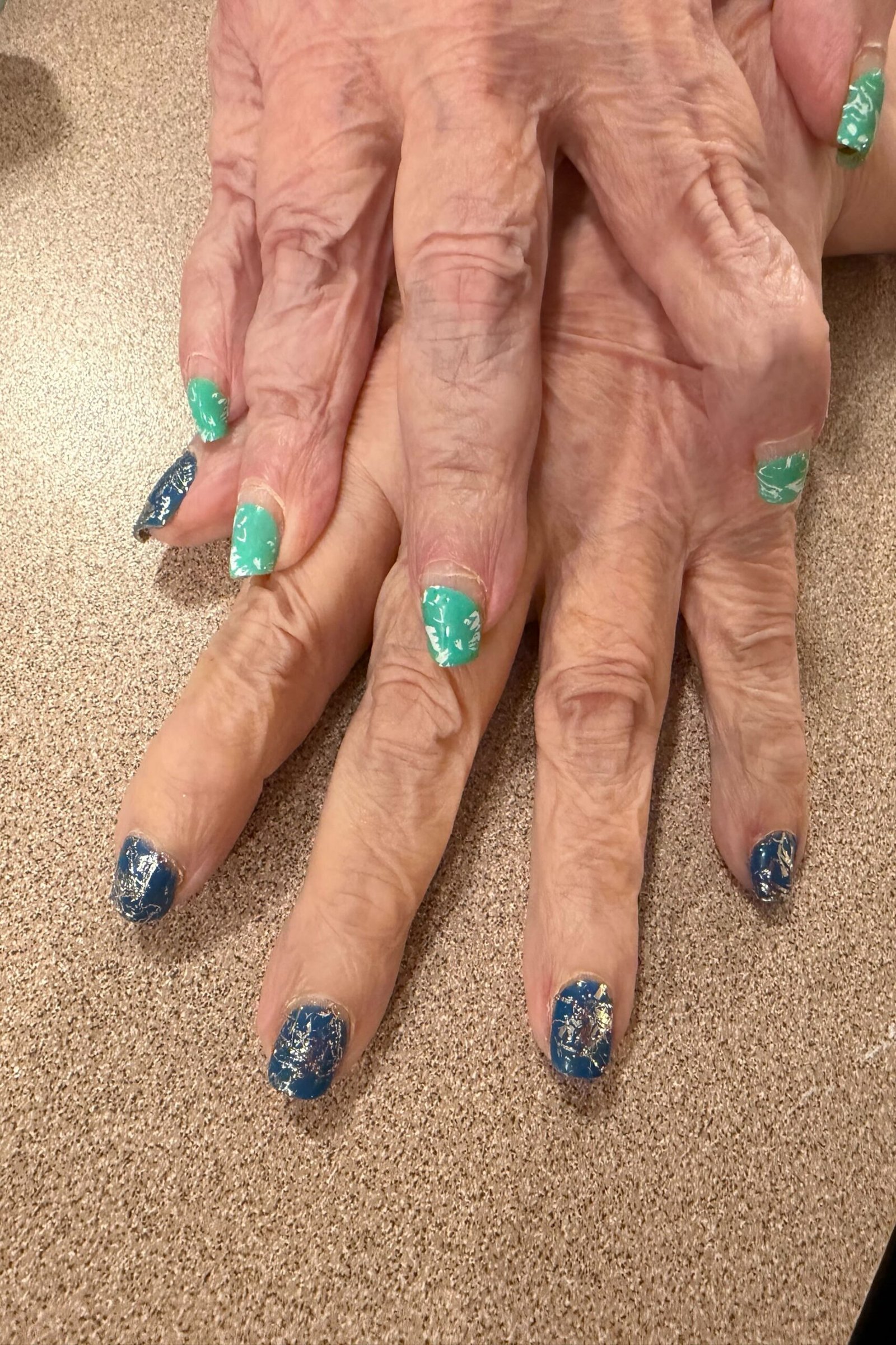 Elderly hands with teal and blue sparkle press-on nails
