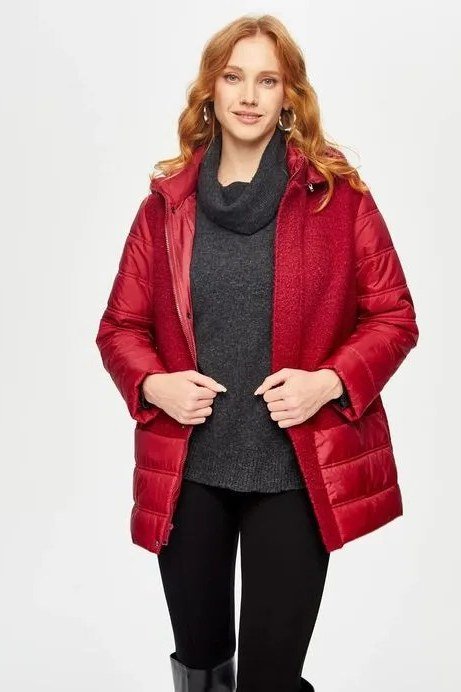 Woman over 60 wearing a red puffer coat open over a gray cowl-neck sweater with black pants