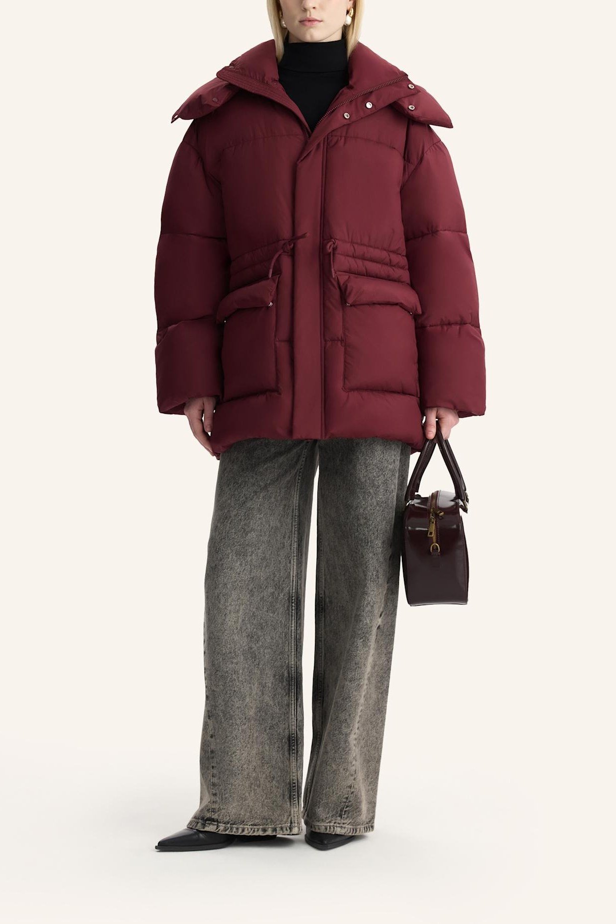 Woman over 60 wearing a burgundy puffer coat over a dark turtleneck with gray wide-leg jeans