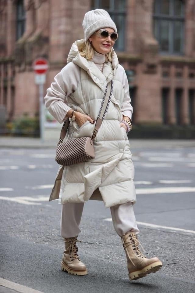 Woman over 60 wearing a cream puffer coat with tan lace-up boots on a city street