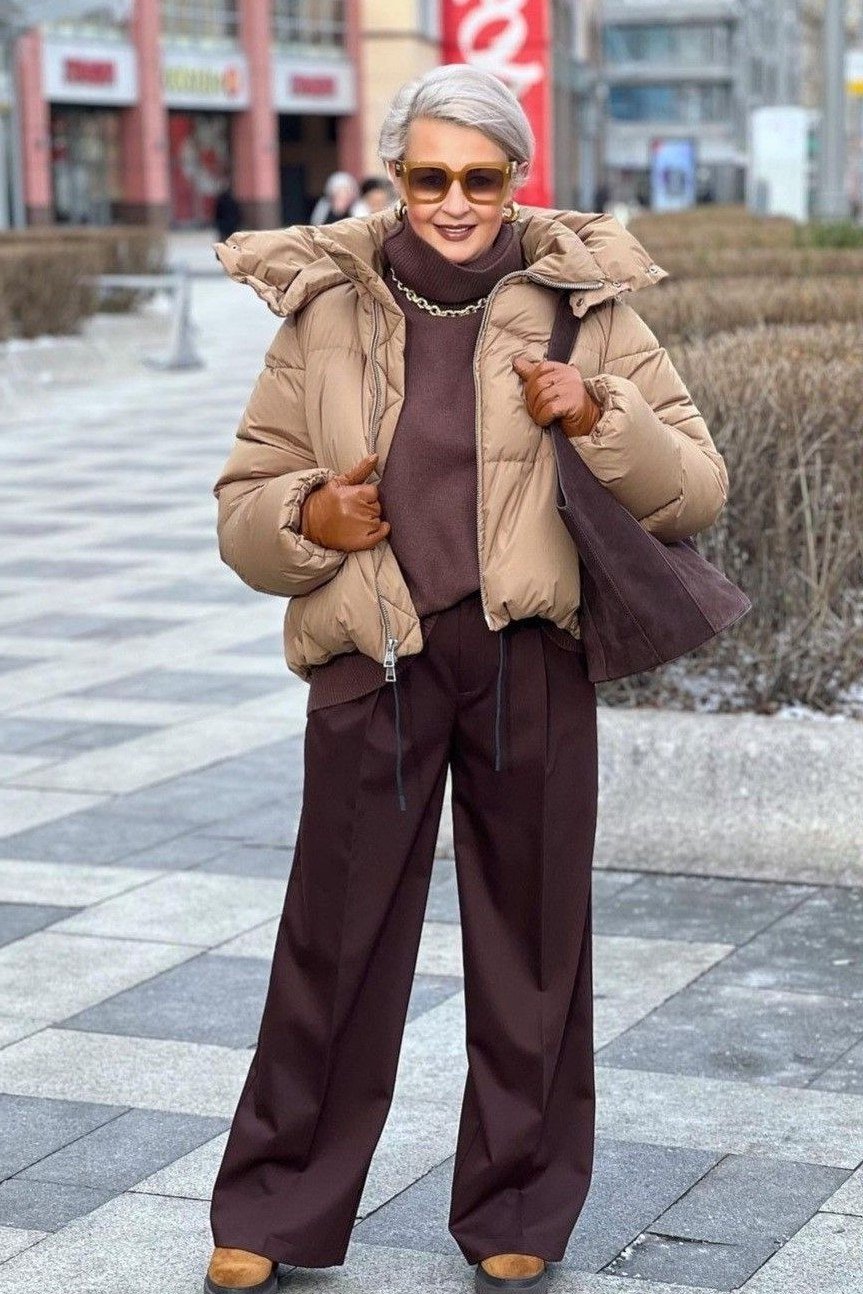 Woman over 60 wearing a camel puffer coat with chocolate-brown wide-leg trousers