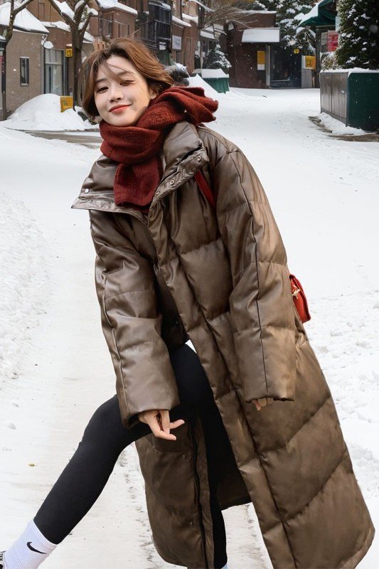 Woman over 60 wearing a bronze long puffer coat with a red scarf over black leggings in the snow