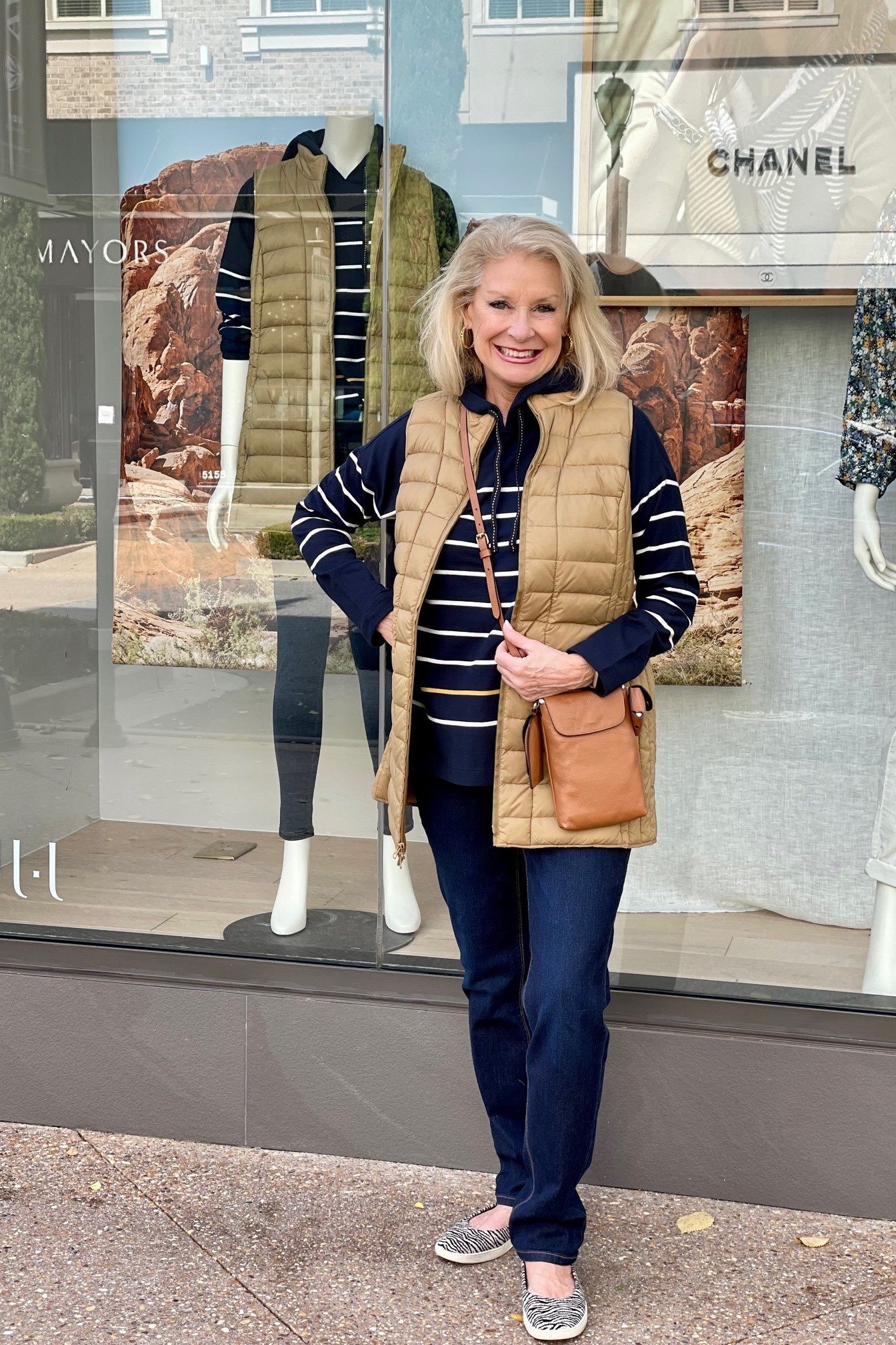Woman over 60 wearing a tan quilted vest over a striped top with blue jeans