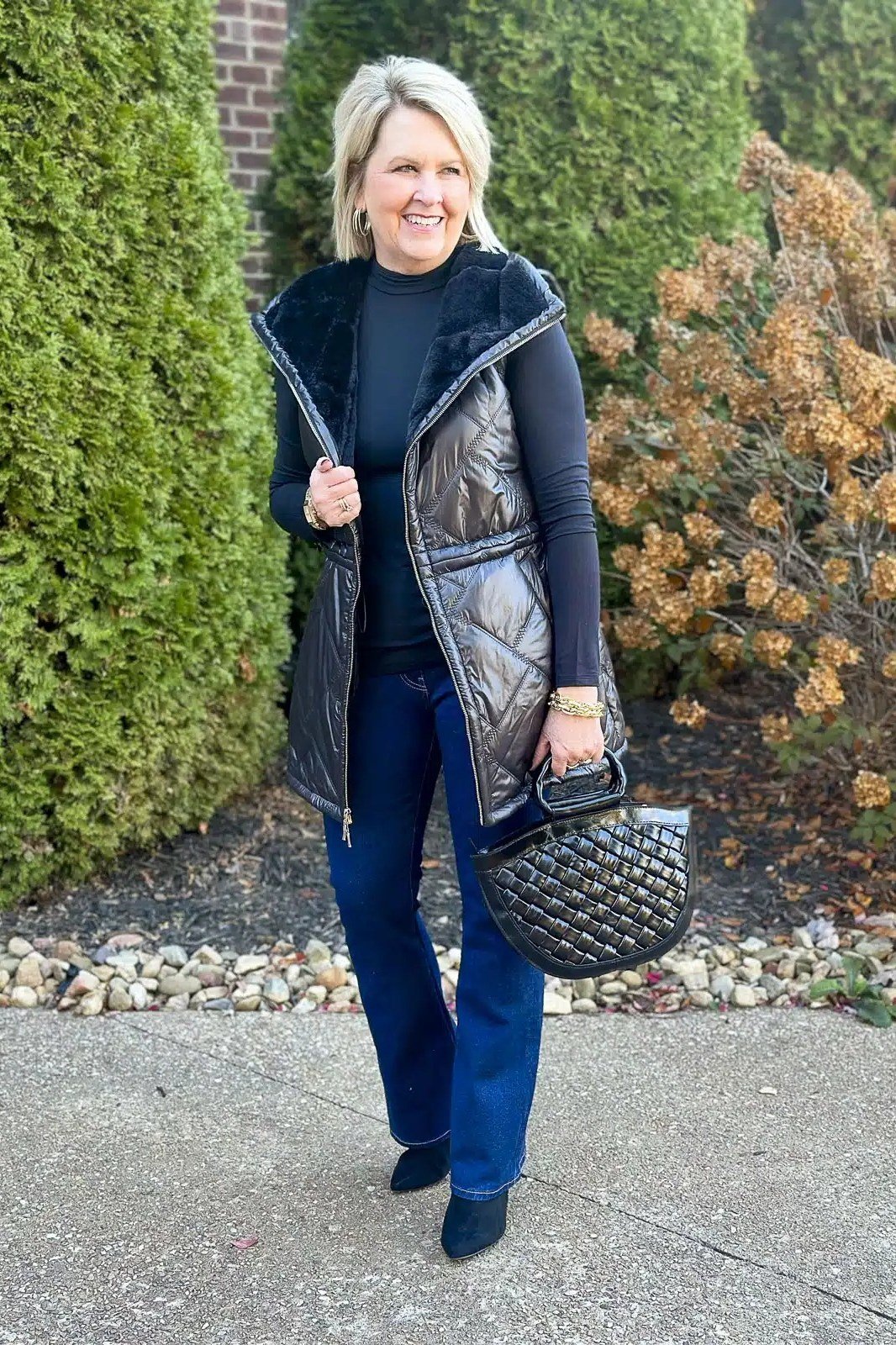 Woman over 60 wearing a silver-gray long vest over blue jeans with a quilted bag