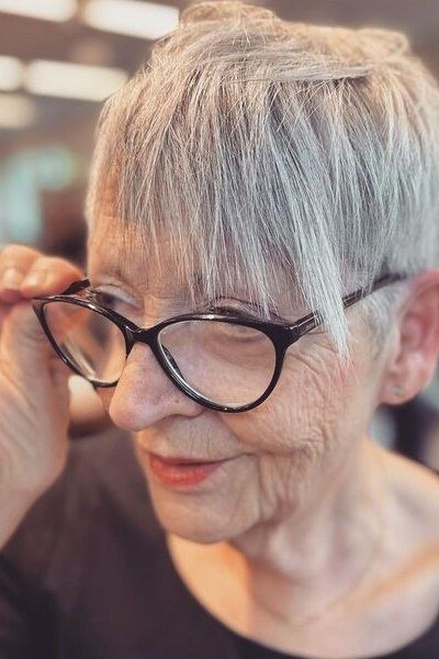 This grey pixie has a soft, piece-y fringe and textured crown, styled with elegant glasses.