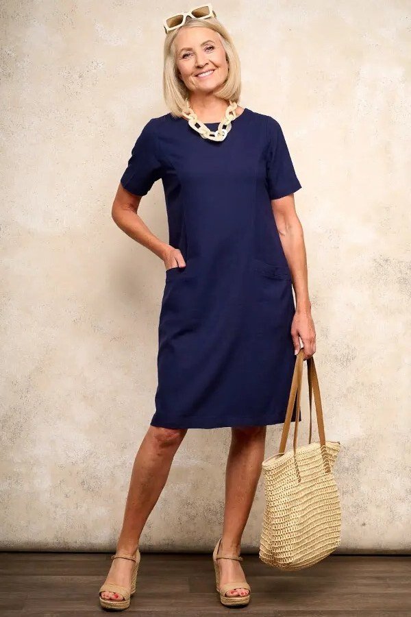 Navy straight shirt dress for women over 60: simple short-sleeve cut with a chunky shell necklace and straw bag
