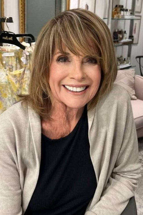 honey blonde shaggy lob with brow-skimming bangs on a smiling woman over 60