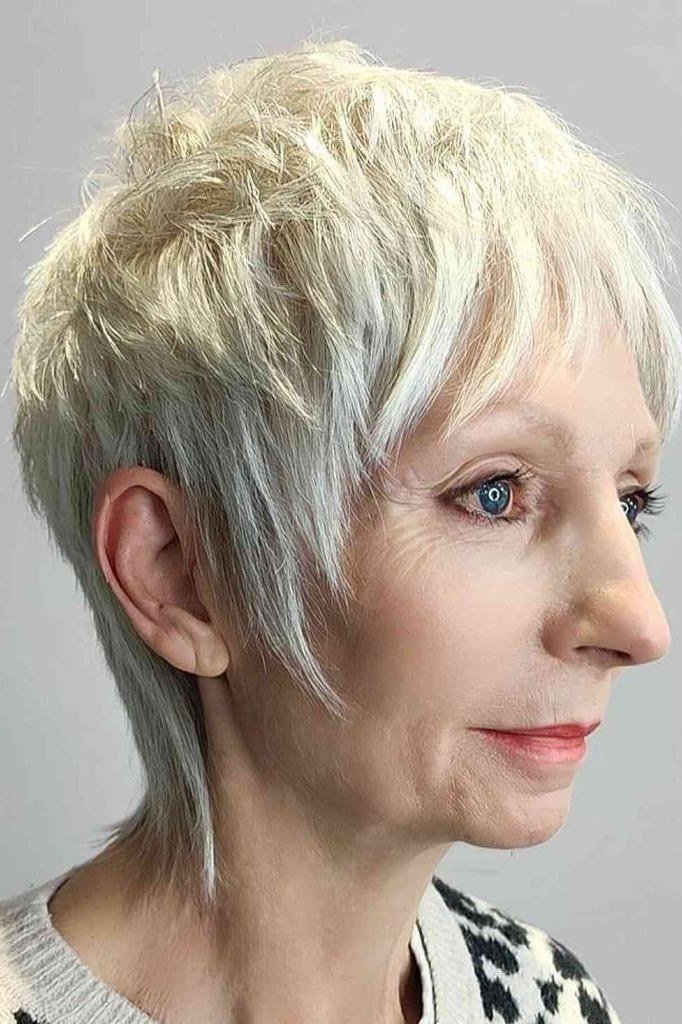 Shaggy pixie bob hairstyle for women over 60: platinum pixie bob with long side bangs, sleek-tapered, side view, older woman