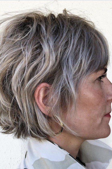 Shaggy pixie bob hairstyle for women over 60: silver wavy shaggy pixie bob, full textured volume, older woman, side view