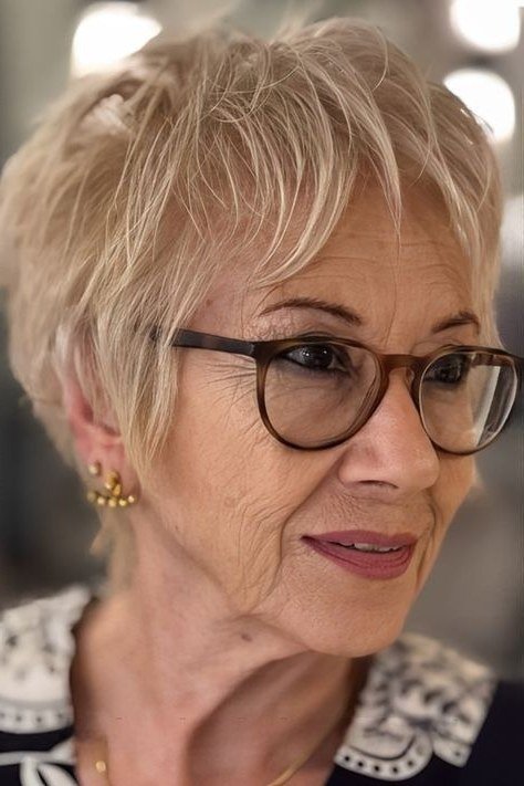 Shaggy pixie bob hairstyle for women over 60: blonde shaggy pixie crop, textured longer top, front view, older woman with glasses