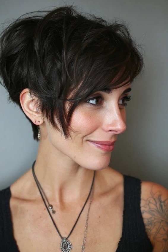 Shaggy pixie bob hairstyle for women over 60: black shaggy pixie bob with bangs, choppy volume, younger woman, front 3/4 view