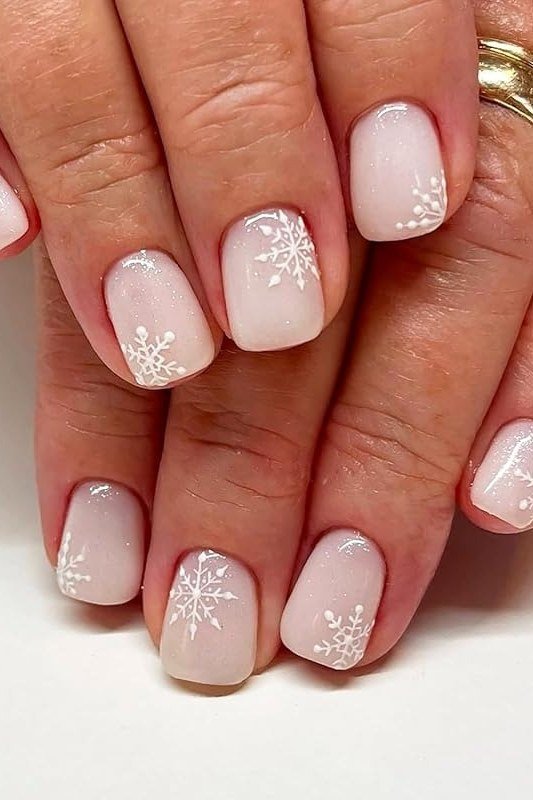 Sheer nude nails with fine white snowflakes on mature hands, graceful winter manicure
