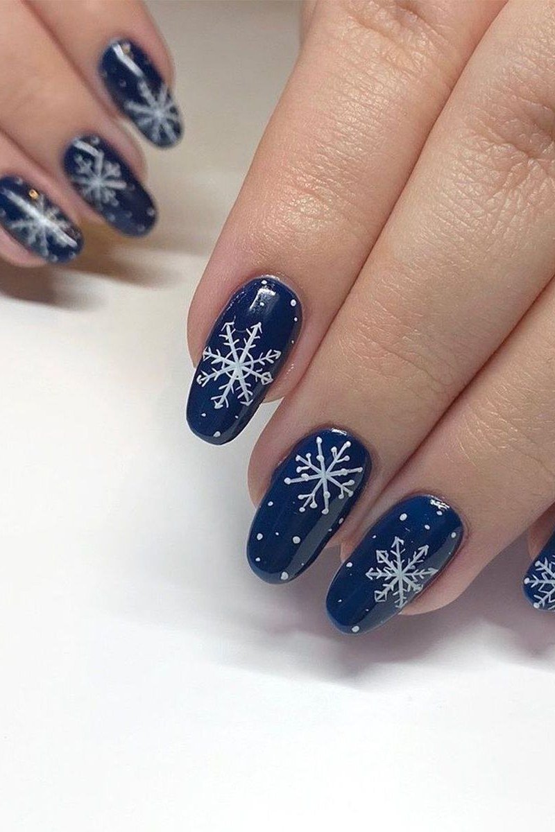 Navy nails with bold graphic white snowflakes, modern winter nail art design