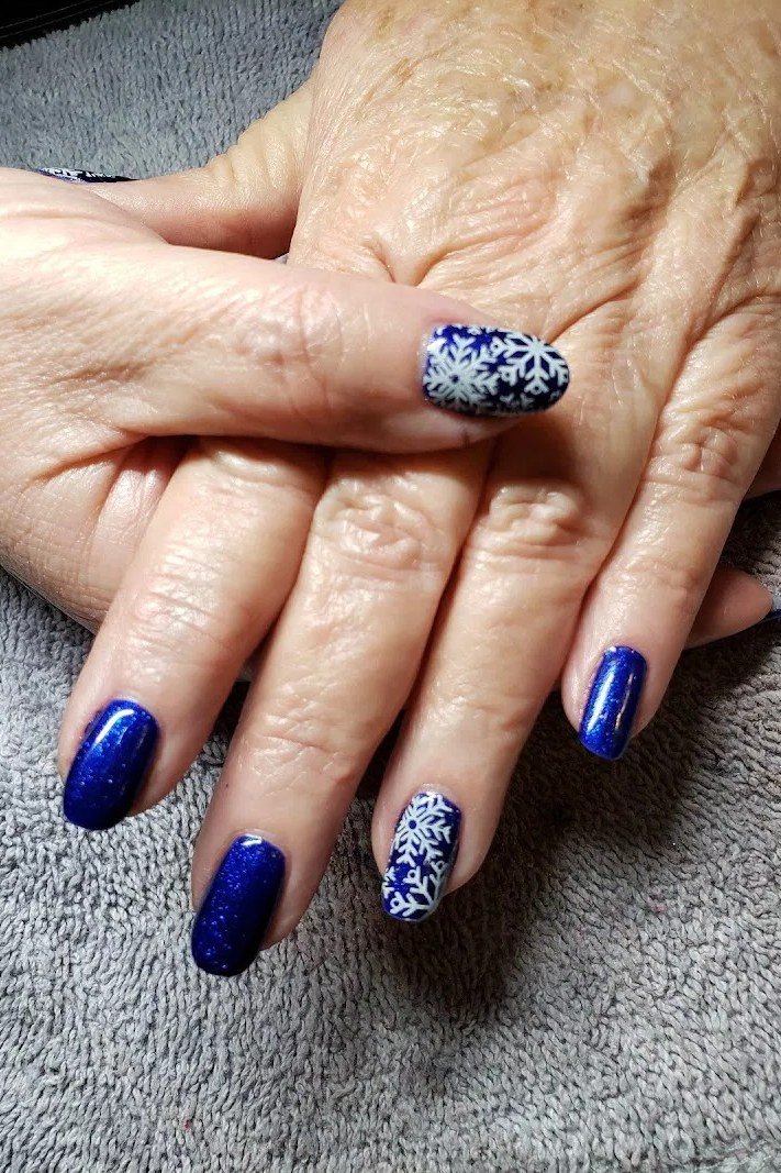 Vivid royal blue nails with white snowflakes on mature hands, regal winter manicure